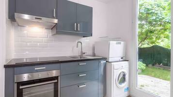 A modern kitchen with grey cabinets, a stainless steel range hood, a built-in oven, a sink, and a front-loading washing machine.