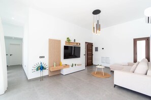 Ein modernes Wohnzimmer mit Flachbildfernseher, einer Wandverkleidung aus Holz, einem weißen Sofa und einem Essbereich mit Holztisch und Stühlen.