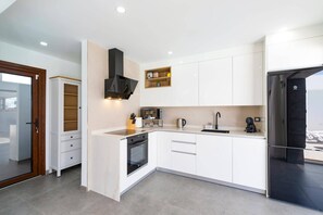 A modern kitchen with white cabinetry, a built-in oven, a black range hood, and a stainless steel refrigerator. - Villa Malvasia Sol by Villa Plus (Playa Blanca)