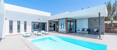 Una casa moderna amb piscina, mobiliari exterior i un mur de pedra.