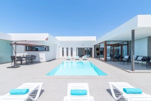 A modern outdoor pool area with lounge chairs and a dining setup. - Villa Malvasia Sol by Villa Plus (Playa Blanca)