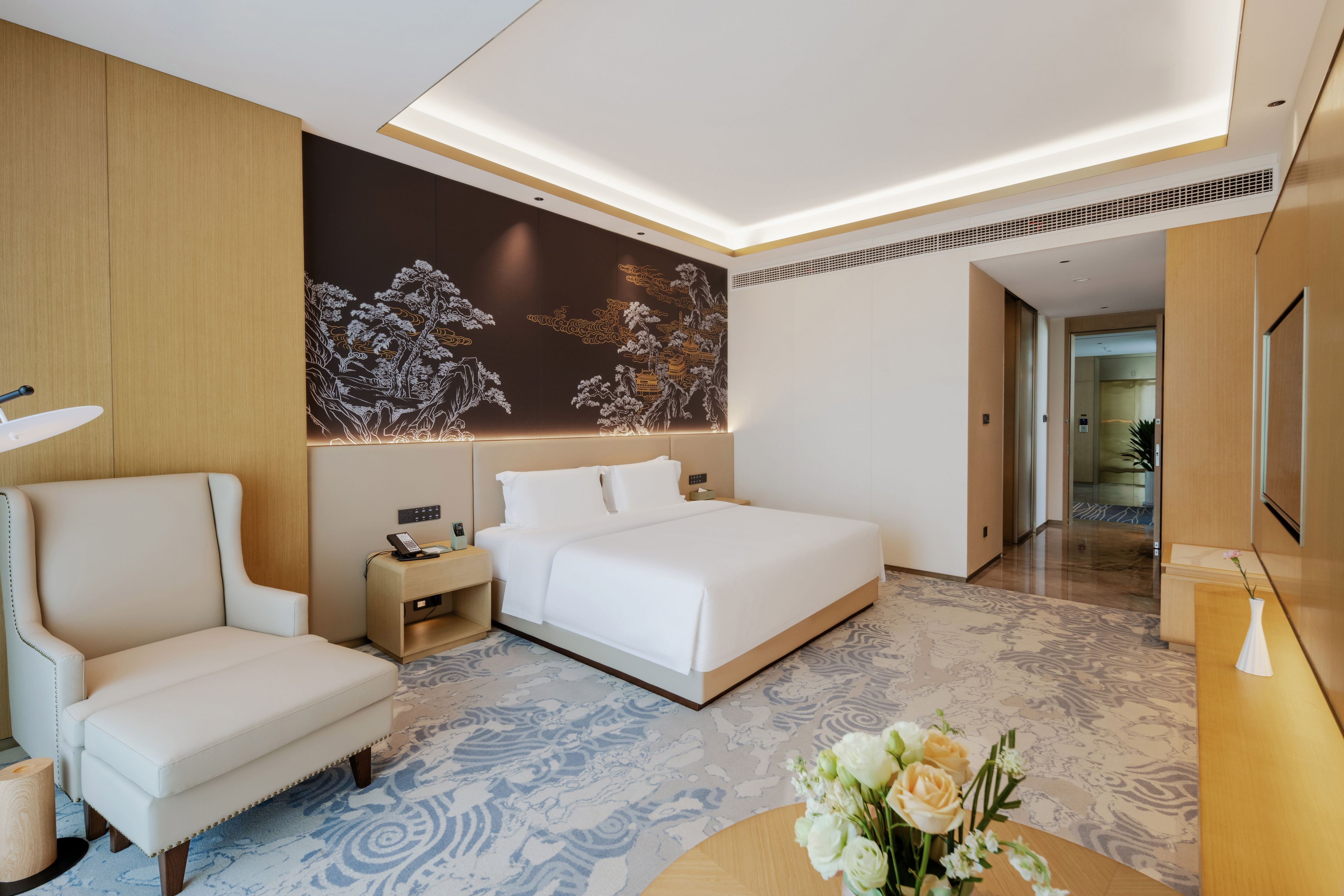 Una habitación de hotel moderna con una cama, una silla, una mesita de noche y un detalle decorativo en la pared.