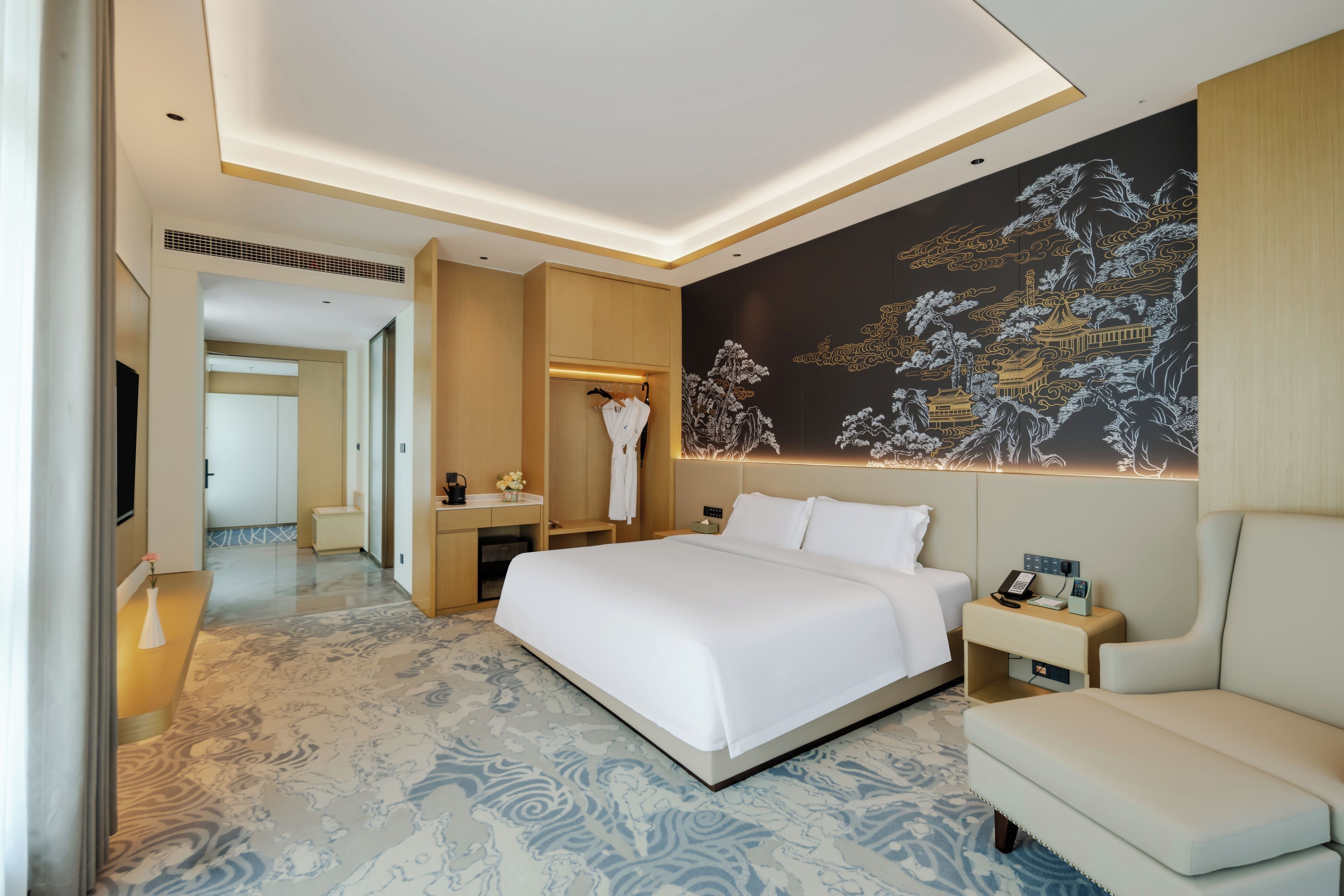 Une chambre d’hôtel avec un grand lit, une table de chevet, une chaise, un bureau et un mur orné d’un tableau traditionnel.