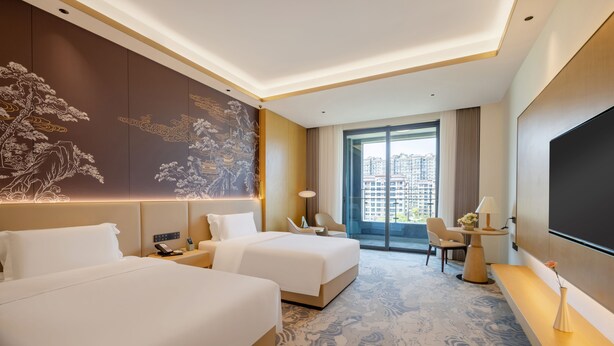A hotel room with two beds, a large wall mural, a balcony with a view of buildings, and a flat-screen TV. - Grand Skylight Hotel Jingdezhen (Jingdezhen)