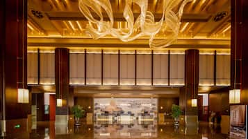 A spacious lobby with a reflective floor, a large decorative light fixture, and a reception desk with seating.