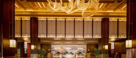 A spacious lobby with a reflective floor, a large decorative light fixture, and a reception desk with seating.