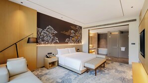 A modern hotel room with a large bed, a bedside table, a lamp, a sofa, and a decorative wall mural. - Grand Skylight Hotel Jingdezhen (Jingdezhen)