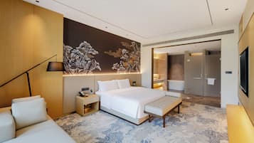 Ein modernes Hotelzimmer mit einem großen Bett, einem Nachttisch, einer Lampe, einer Couch und einer dekorativen Wandmalerei.