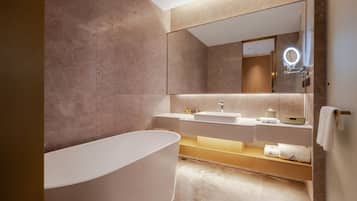 A modern bathroom with a freestanding bathtub, a large mirror with a round light, and a vanity with a sink and towel rack.