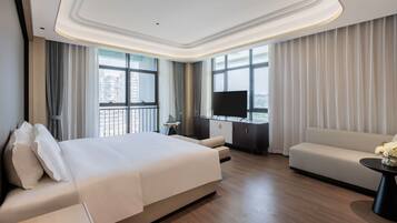 A modern hotel room with a large bed, a sofa, a TV, and a balcony with curtains.