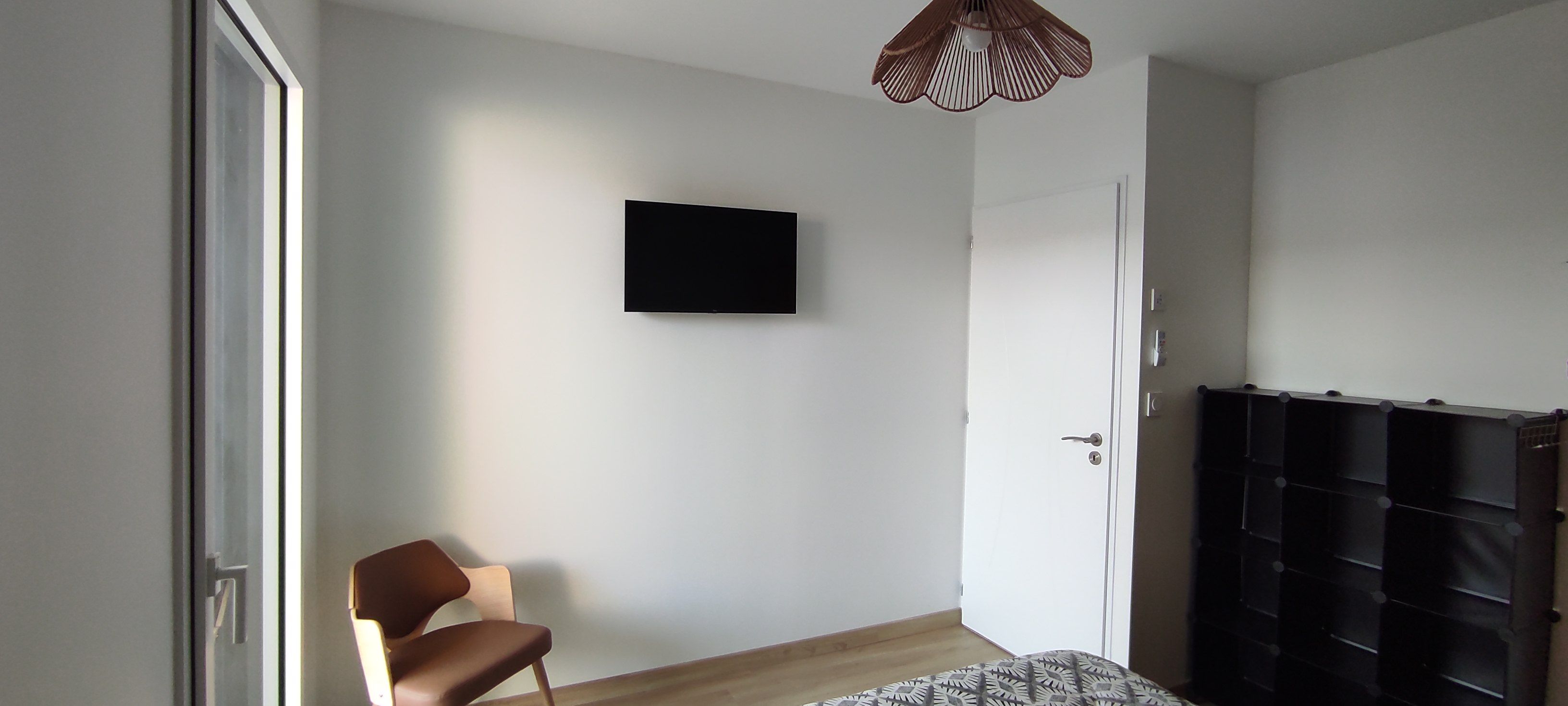 A room with a bed, a chair, a television mounted on the wall, and a wardrobe with multiple compartments.