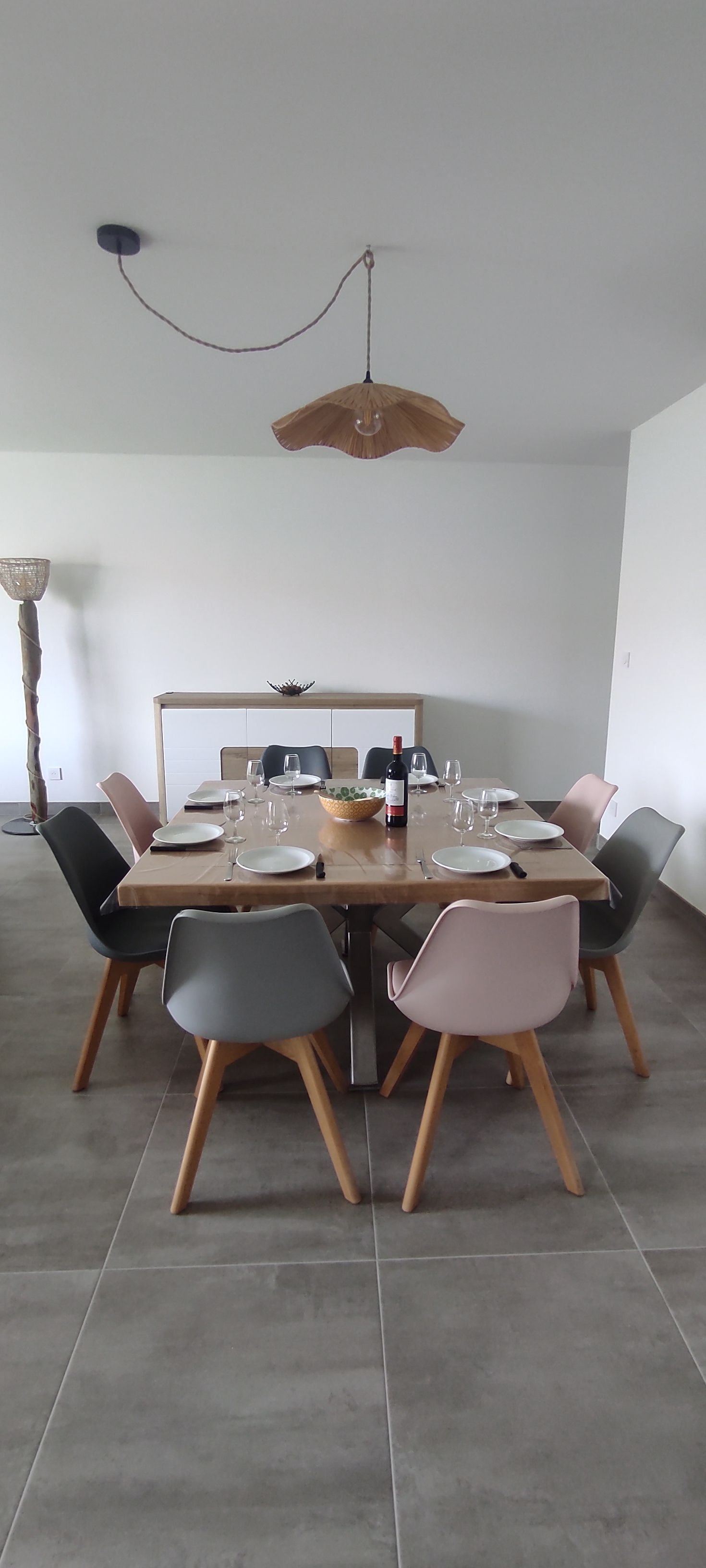 A dining area with a rectangular table set for six, surrounded by six chairs with wooden legs.