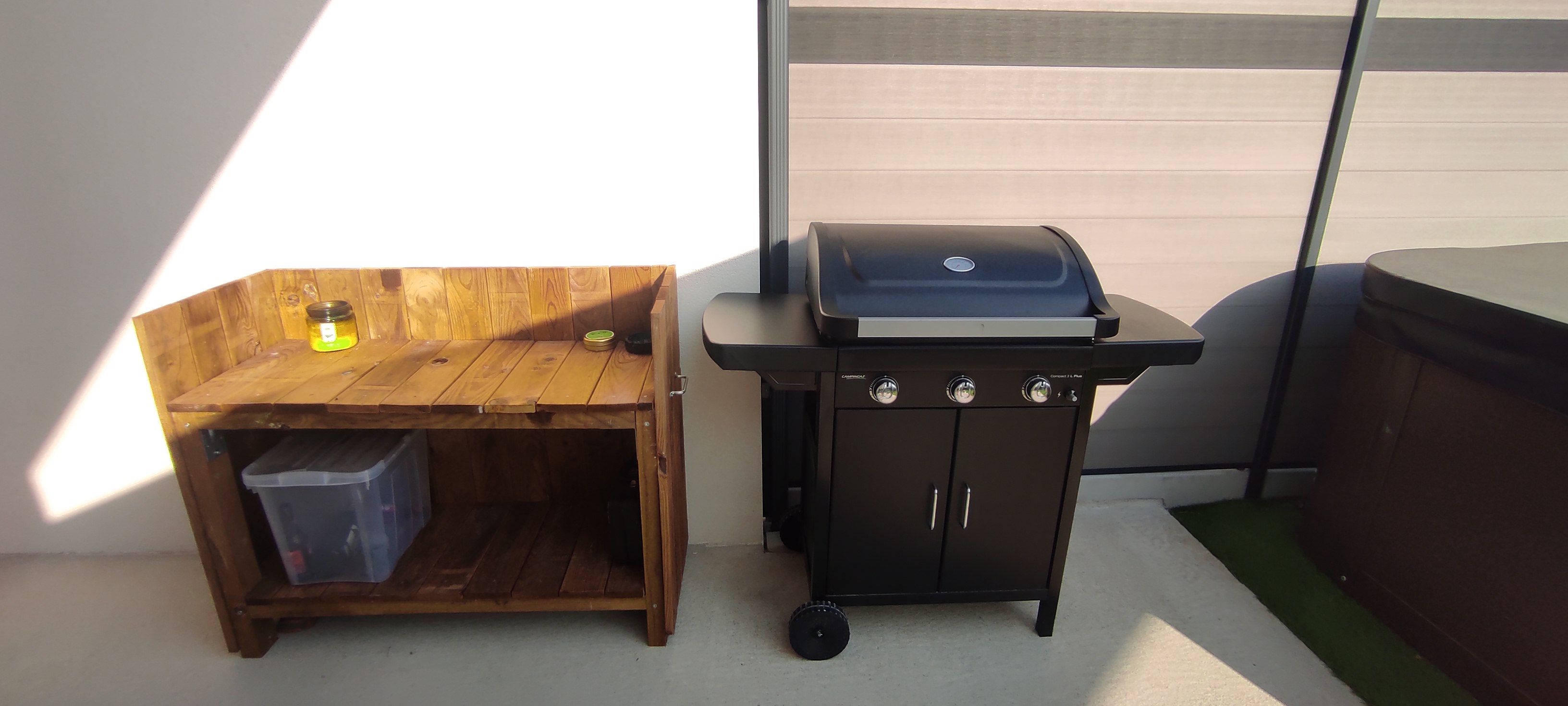 A wooden bench with a trash bin and a barbecue grill.