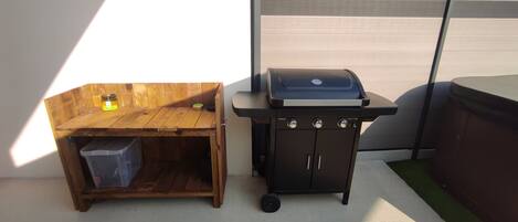 A wooden bench with a trash bin and a barbecue grill.