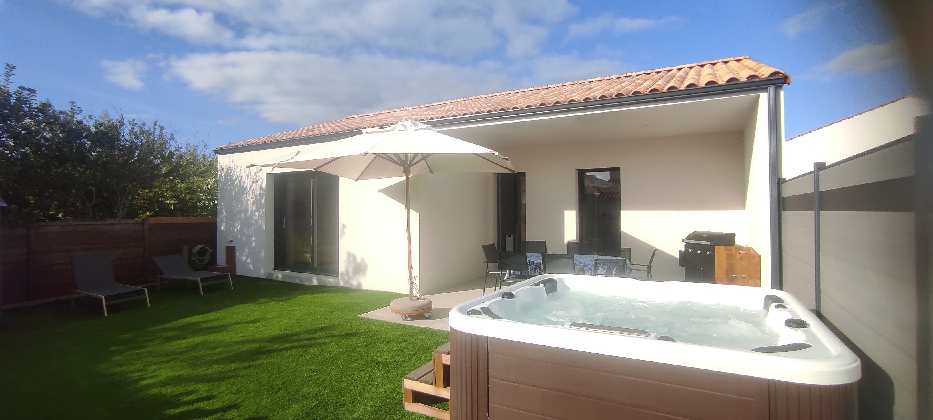 A backyard with a hot tub, a covered patio area, and a small seating area with chairs and an umbrella.