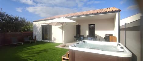 A backyard with a hot tub, a covered patio area, and a small seating area with chairs and an umbrella.