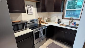 A kitchen with dark cabinets, a stainless steel refrigerator, a microwave, an oven, and a window providing a view of the outdoors.