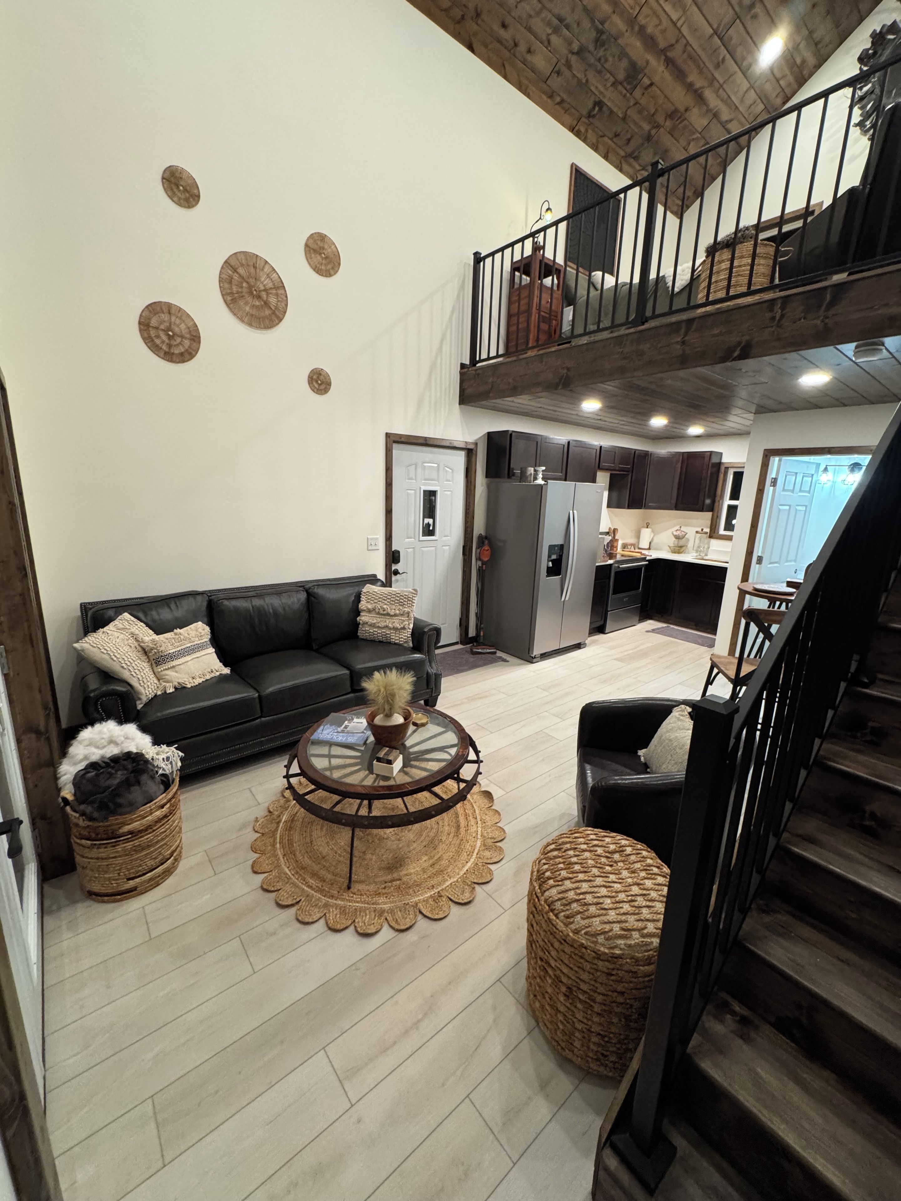 A spacious living area with a black leather sofa, a round coffee table, and a staircase leading to an upper level.