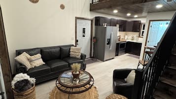 A spacious living area with a black leather sofa, a round coffee table, and a staircase leading to an upper level.