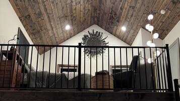 Quarto estilo loft com teto de madeira, varanda com guarda-corrimão preto e área de jantar com mesa redonda.