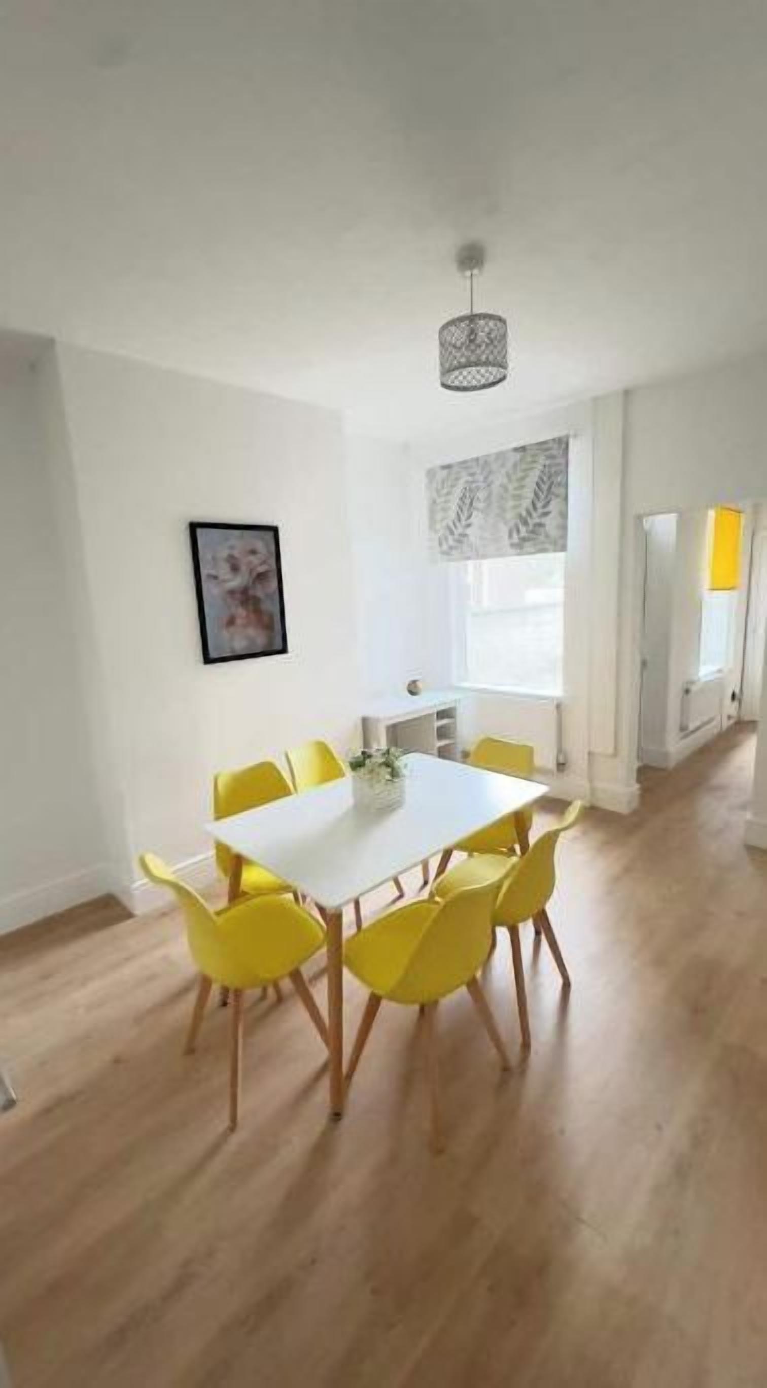 A dining area with a white table and yellow chairs, a hanging light fixture, and a window with a view.