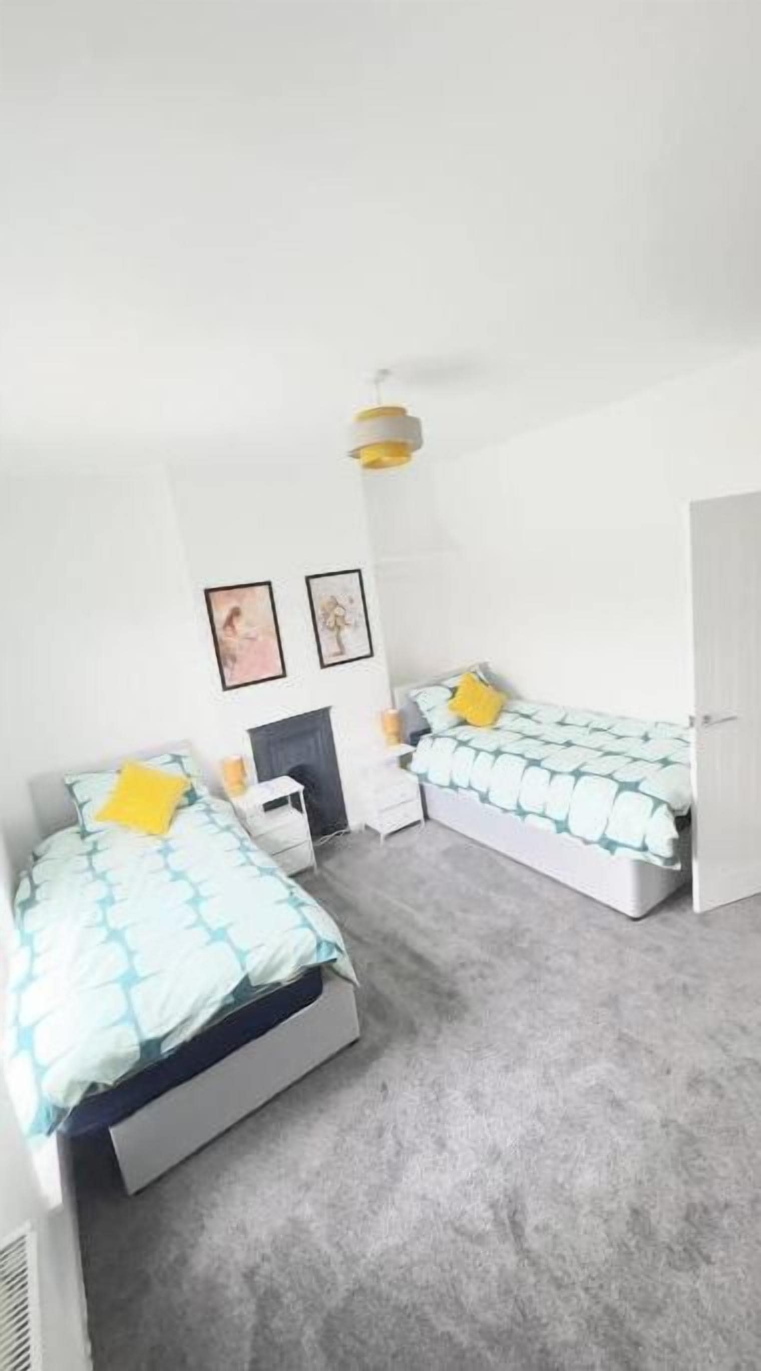 Une chambre avec deux lits, une petite table de chevet, une étagère fixée au mur et une porte.