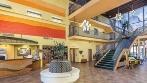 A hotel lobby with a reception desk, a circular seating area, a staircase, and a large window. - WM BLOCK Plaza Resort and Spa 1br (Palm Springs)