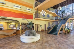 Un hall de hotel con mostrador de recepción, una zona de estar circular, una escalera y un ventanal grande.
