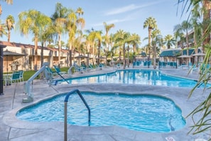 Un área de piscina con varias piscinas, sillas de descanso y palmeras.