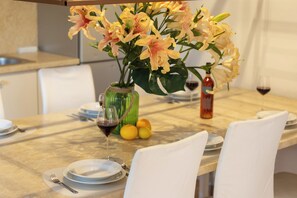 A dining table set with white plates, silverware, and a glass of red wine. There are yellow flowers in a green vase and a bottle of red wine on the table. - Spacious 9-bedroom house with pool and cinema (Kaštel Novi)