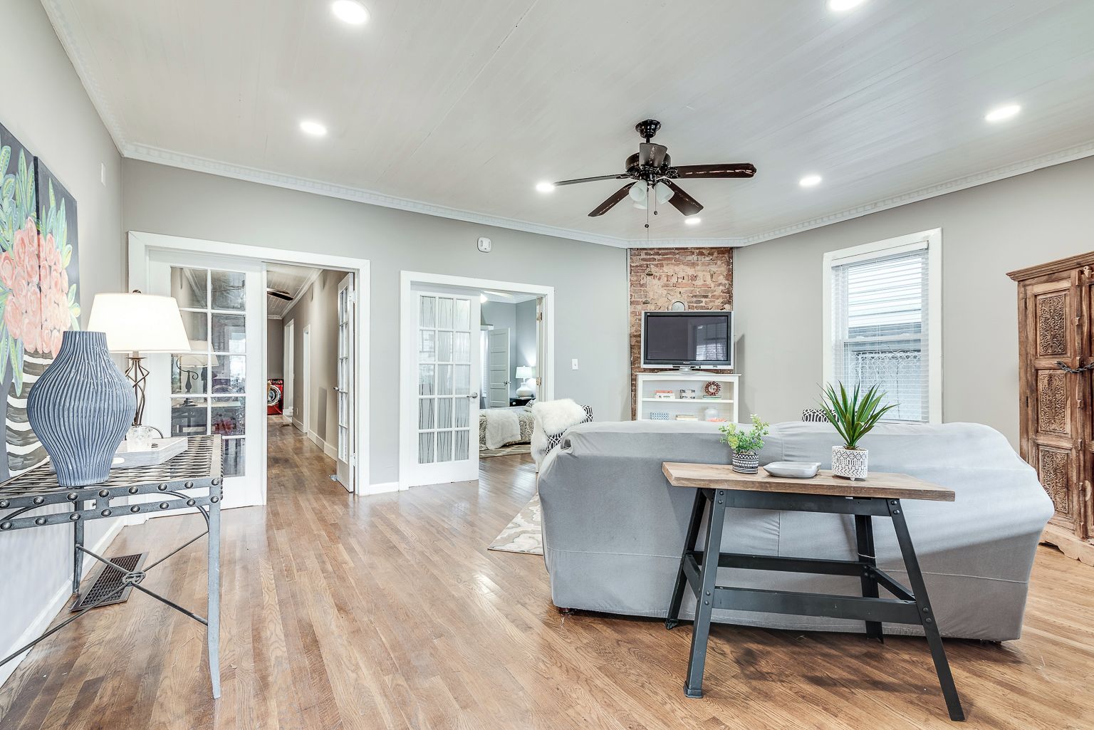 A spacious living area with hardwood flooring, a grey sofa, a wooden coffee table, and a ceiling fan.