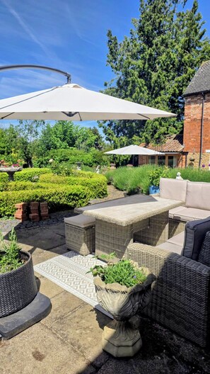 Un'area patio all'aperto con mobili in vimini, un ombrellone bianco e un edificio in mattoni sullo sfondo.