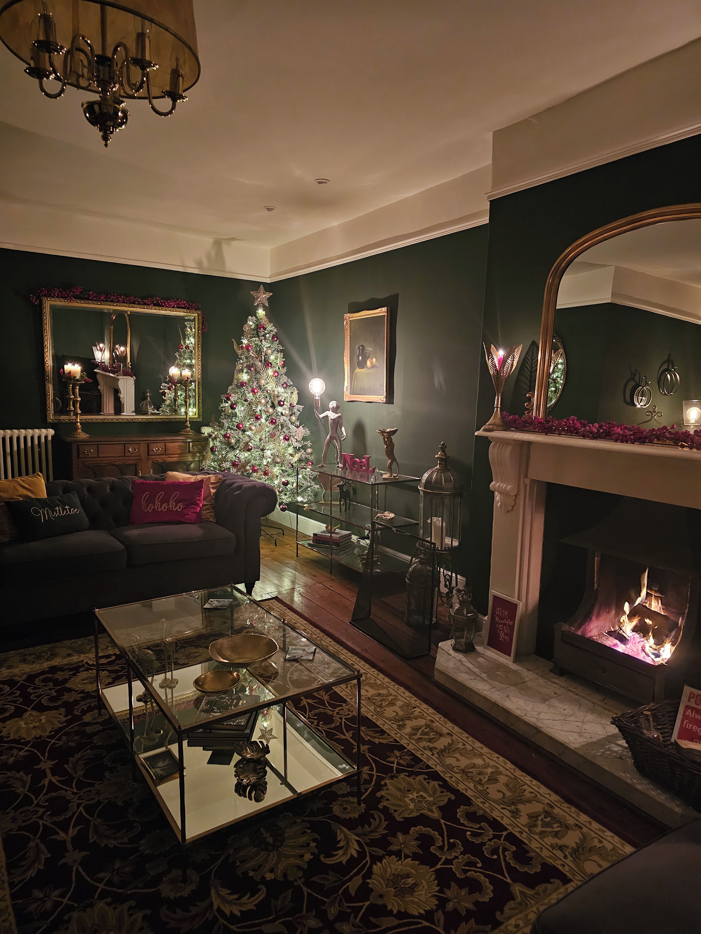 A cozy living room with a fireplace, a Christmas tree, and a large mirror.