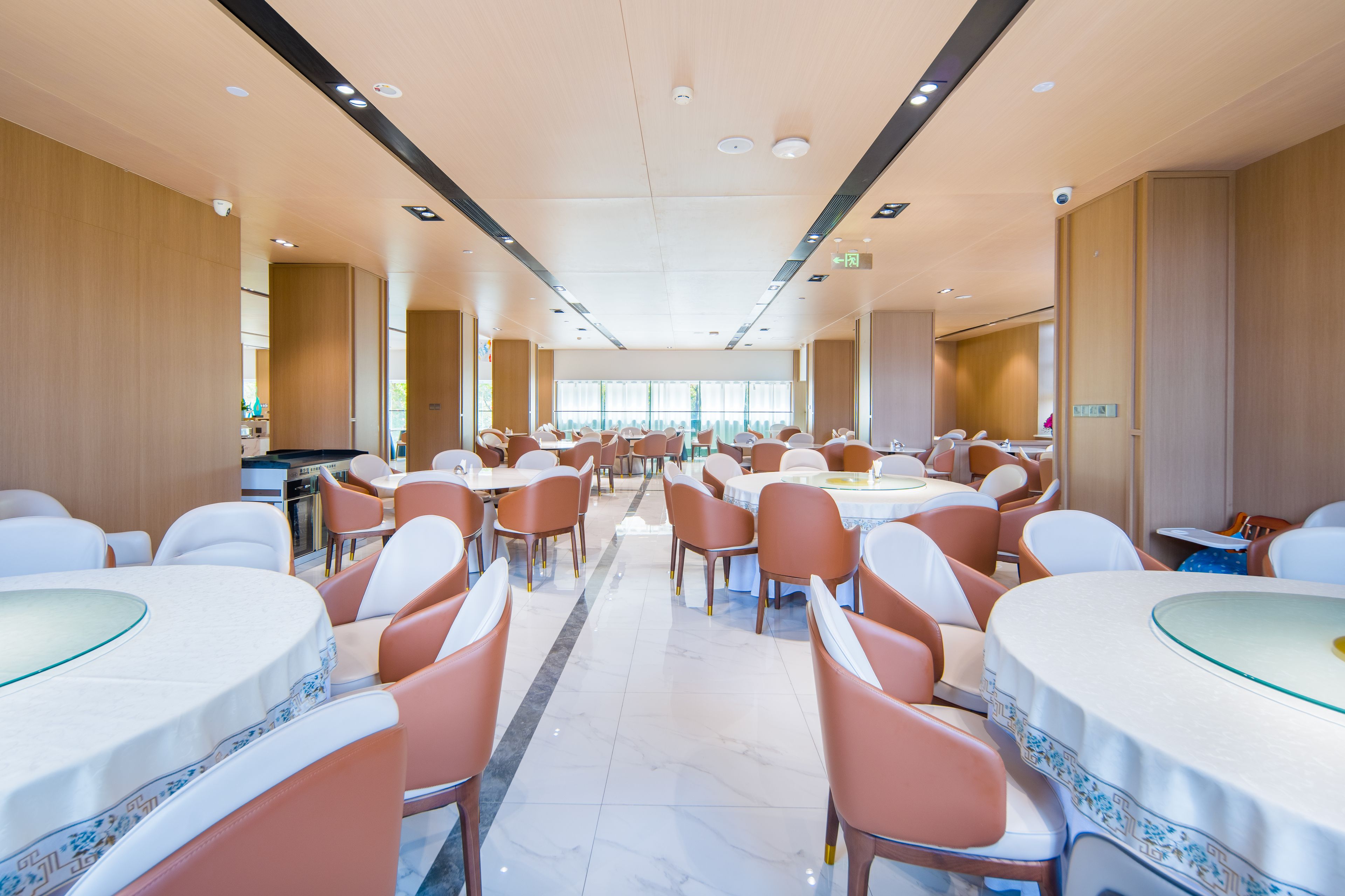 A spacious dining area with round tables and chairs, a clean floor, and a high ceiling with recessed lighting.