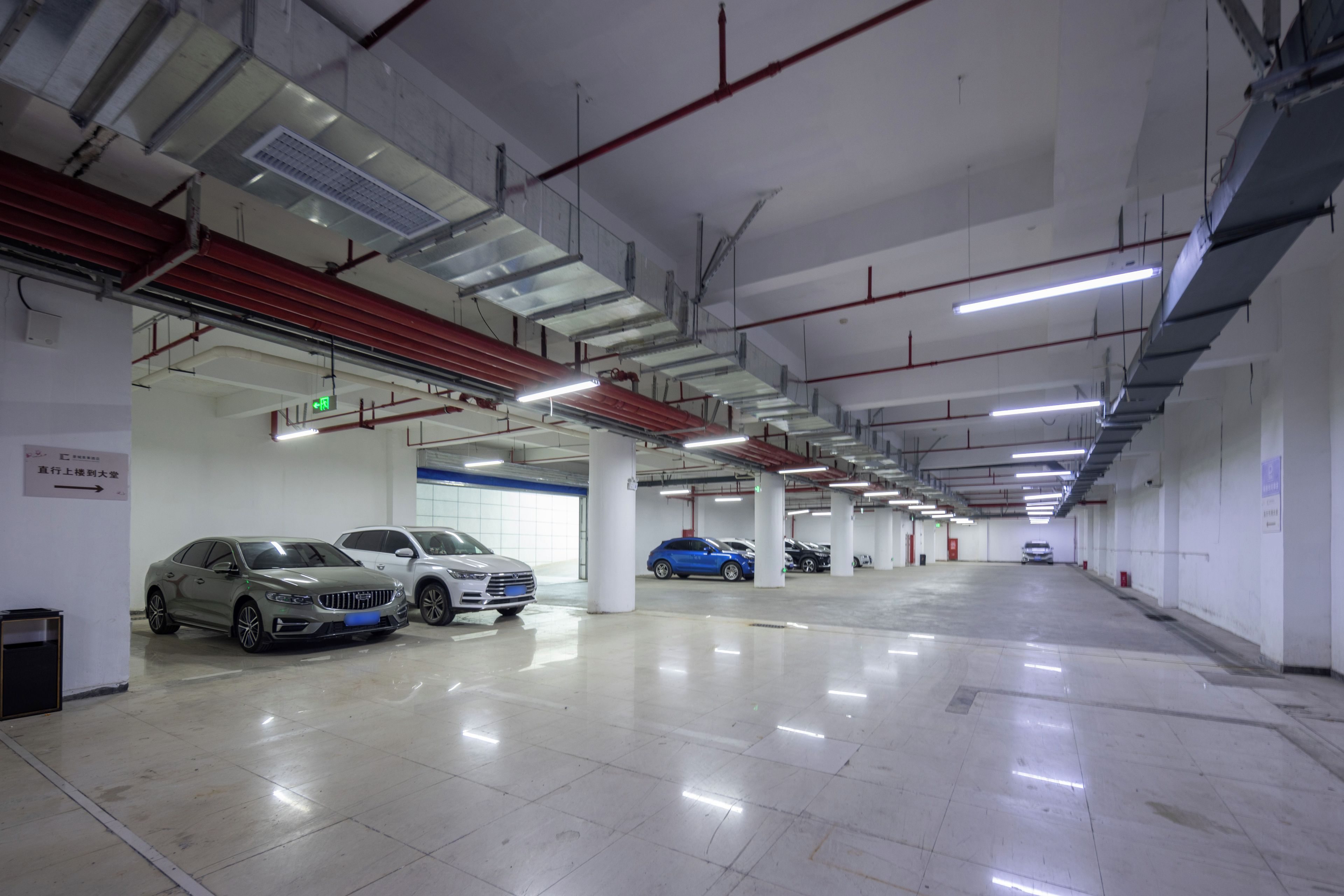 Garagem de estacionamento com vários andares, diversos carros estacionados, sinalização clara e ambiente limpo e bem iluminado.