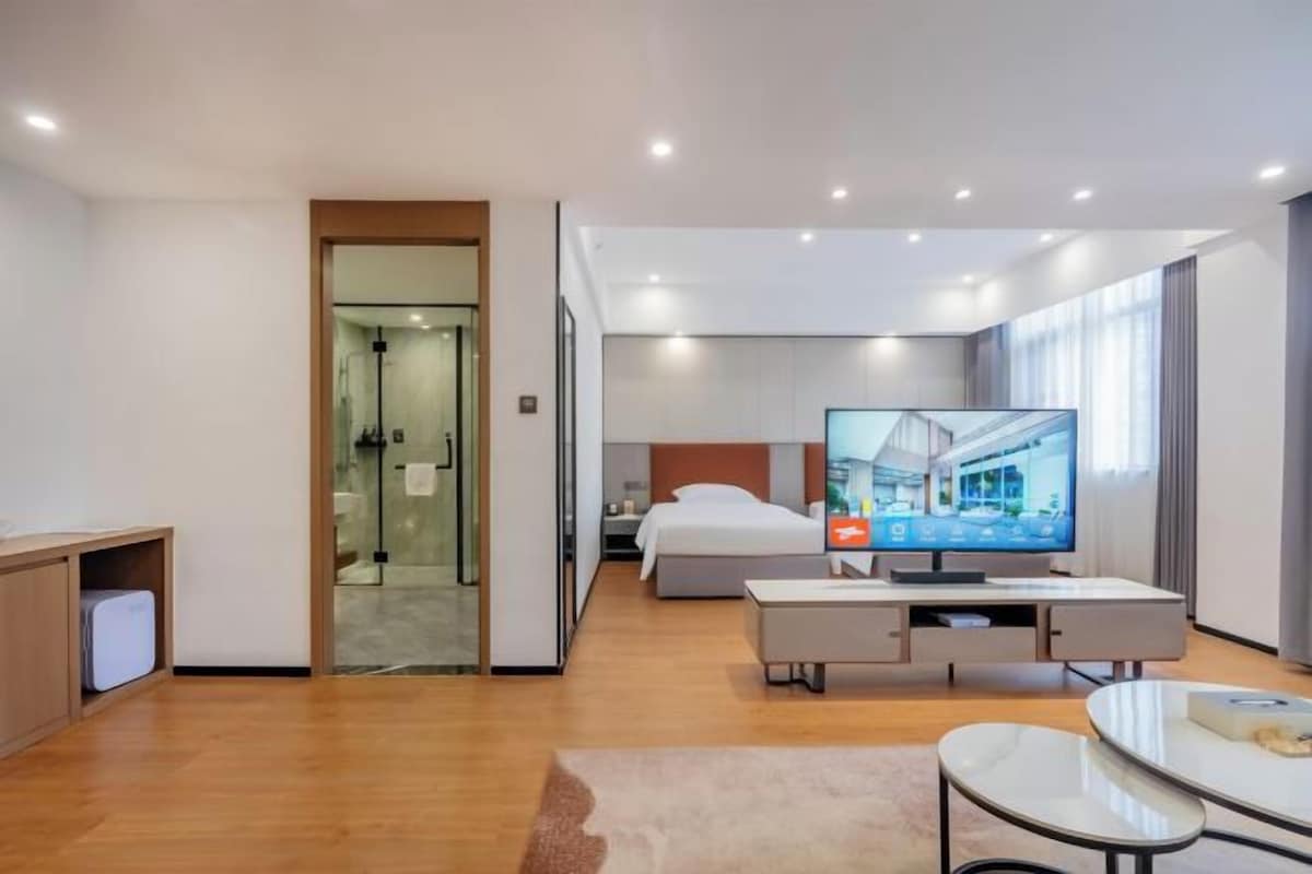 Una habitación de hotel moderna con cama, televisión, escritorio y una puerta de vidrio que da al baño.
