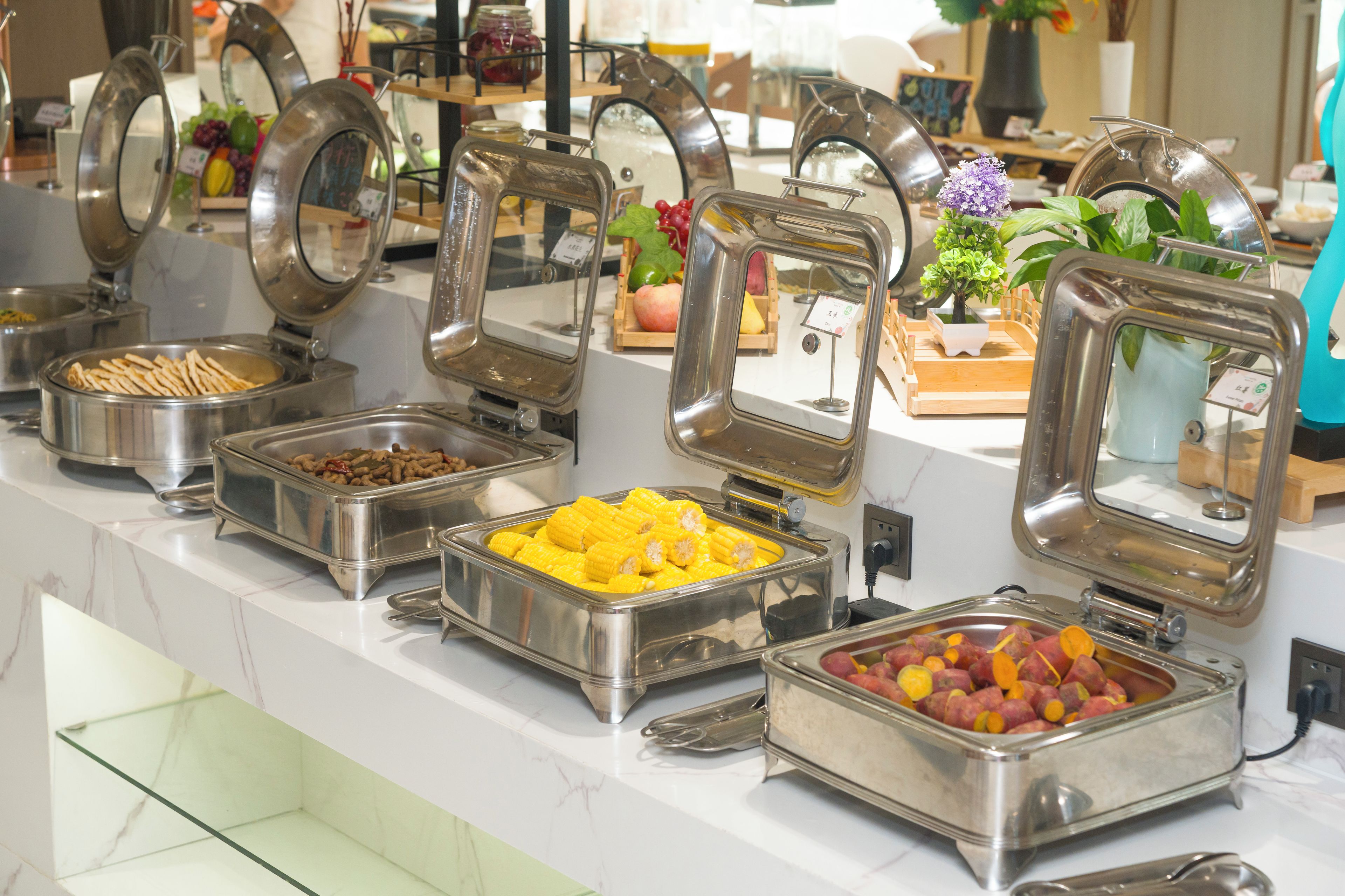 Un bufé con diversos alimentos en recipientes metálicos.