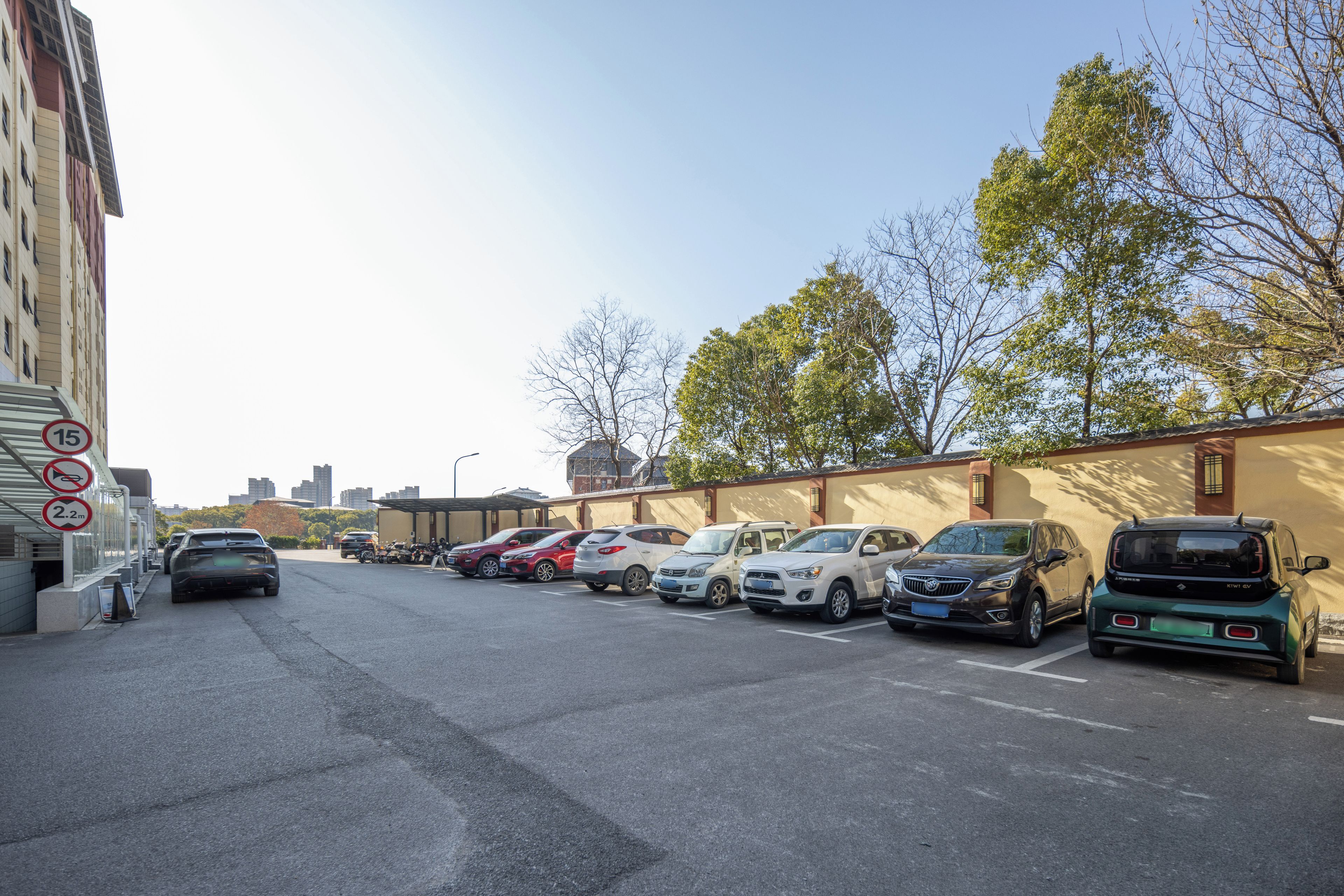 A parking lot with multiple cars and a building with a beige wall and windows.