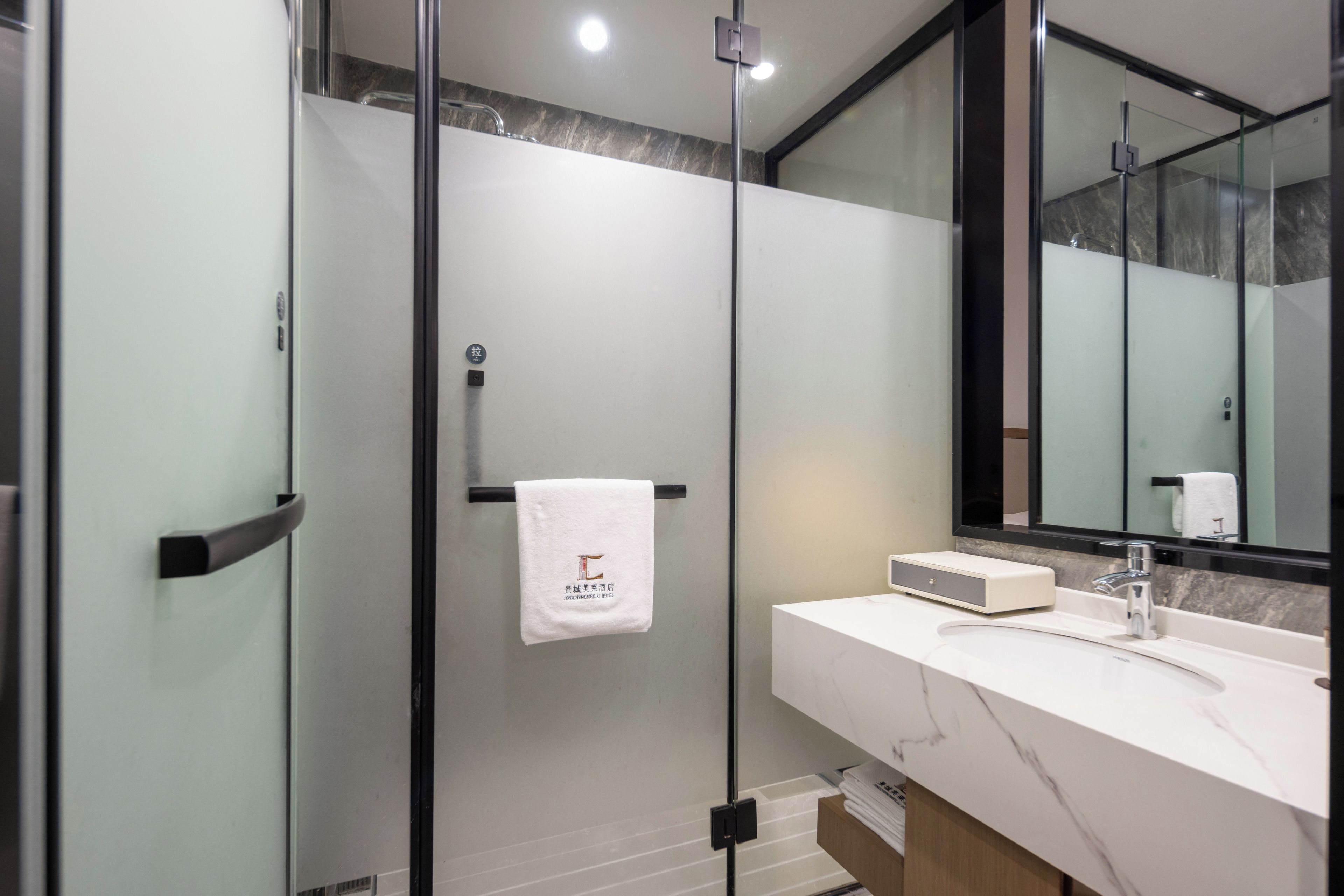 Ein modernes Badezimmer mit einer ein Glasfach raumseitig abgetrennten Dusche, einem weißen Waschbecken mit Marmorplatte und einem großen Spiegel.