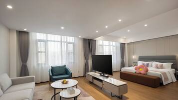 Quarto de hotel moderno com sofá, mesa de jantar, televisão, cama e uma janela grande.