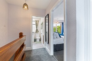 A hallway leading to a bedroom with a bed, a window, and a door. - House Sleeps 7 With Enclosed Garden (Coventry)