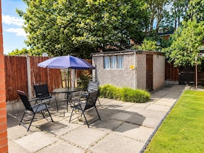 A patio with a table and chairs, a small shed, and a wooden fence. - House Sleeps 7 With Enclosed Garden (Coventry)