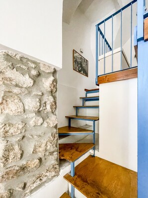 A staircase with wooden steps and blue railings, leading to a landing with a stone wall and a framed picture. - Pierina's Almond Tree (Vitulano)