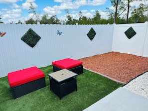 A backyard with a white fence, artificial grass, a wooden table, and two red cushioned benches.