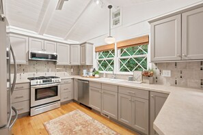 A modern kitchen with stainless steel appliances, grey cabinetry, and a large window with a view of greenery.