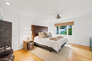 A bedroom with a large bed, a ceiling fan, a window with a view, and a wooden floor. - 4-bedroom home on the Misty Mountain in gorgeous Blowing Rock! (Blowing Rock)