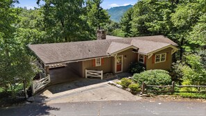 A two-story house with a garage, surrounded by trees and a mountain in the background. - 4-bedroom home on the Misty Mountain in gorgeous Blowing Rock! (Blowing Rock)