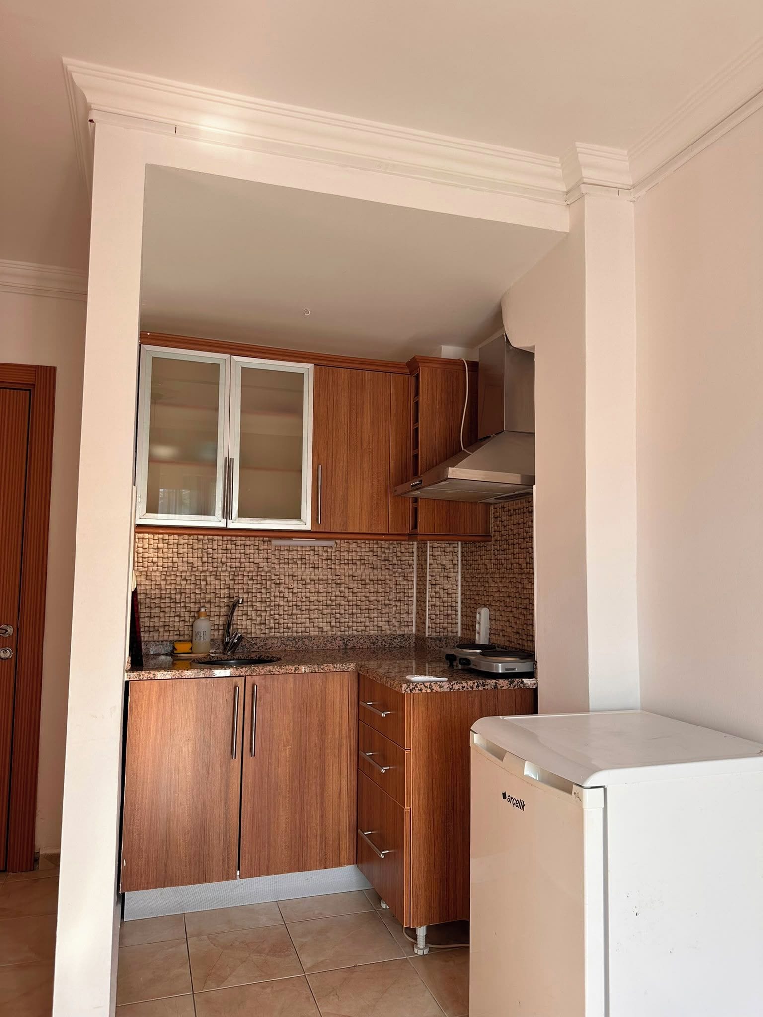 Eine kleine Küche mit Holzschränken, einem eingebauten Ofen und einem weißen Kühlschrank.