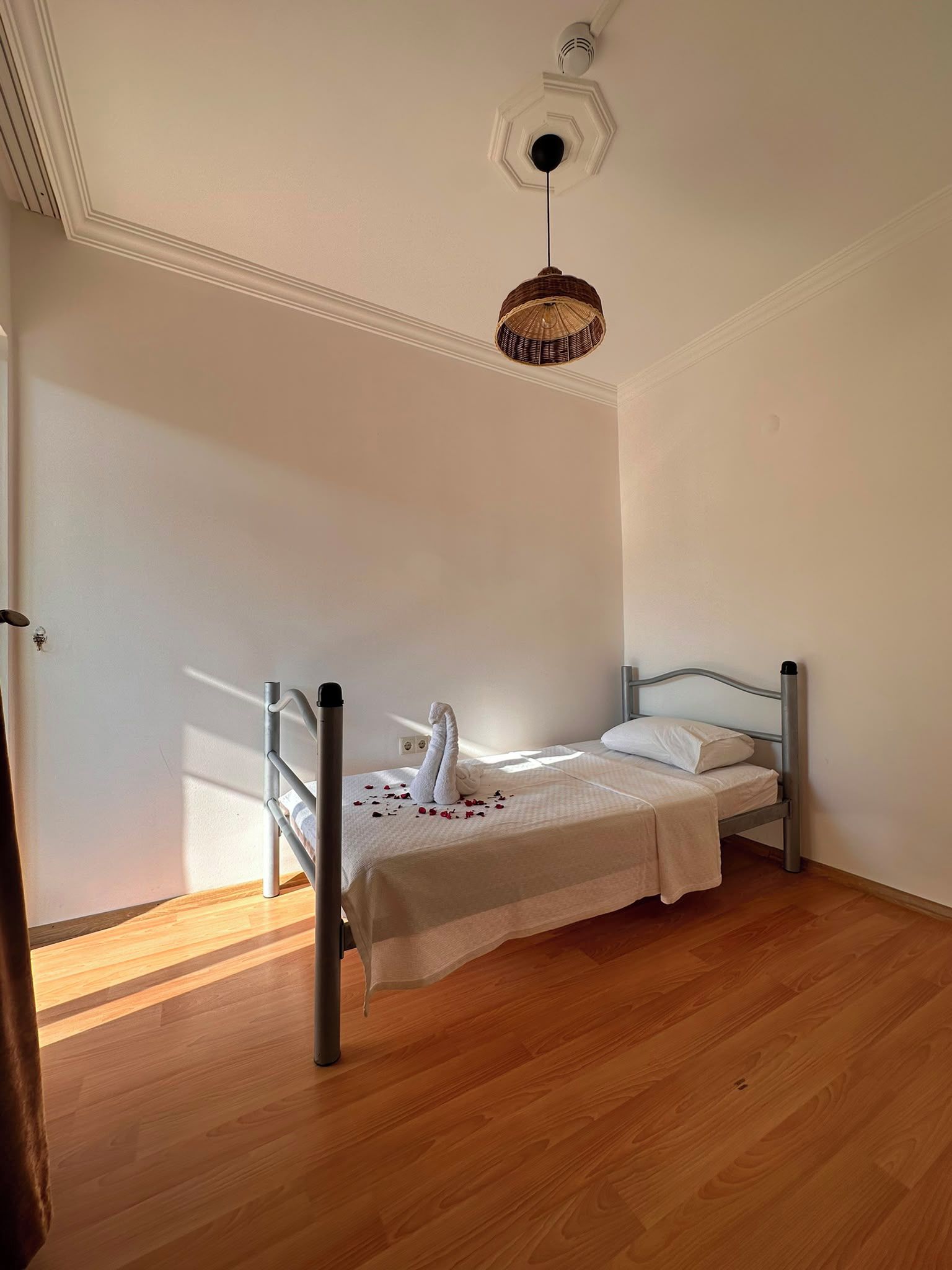 A bedroom with a bed, a hanging light fixture, and wooden flooring.