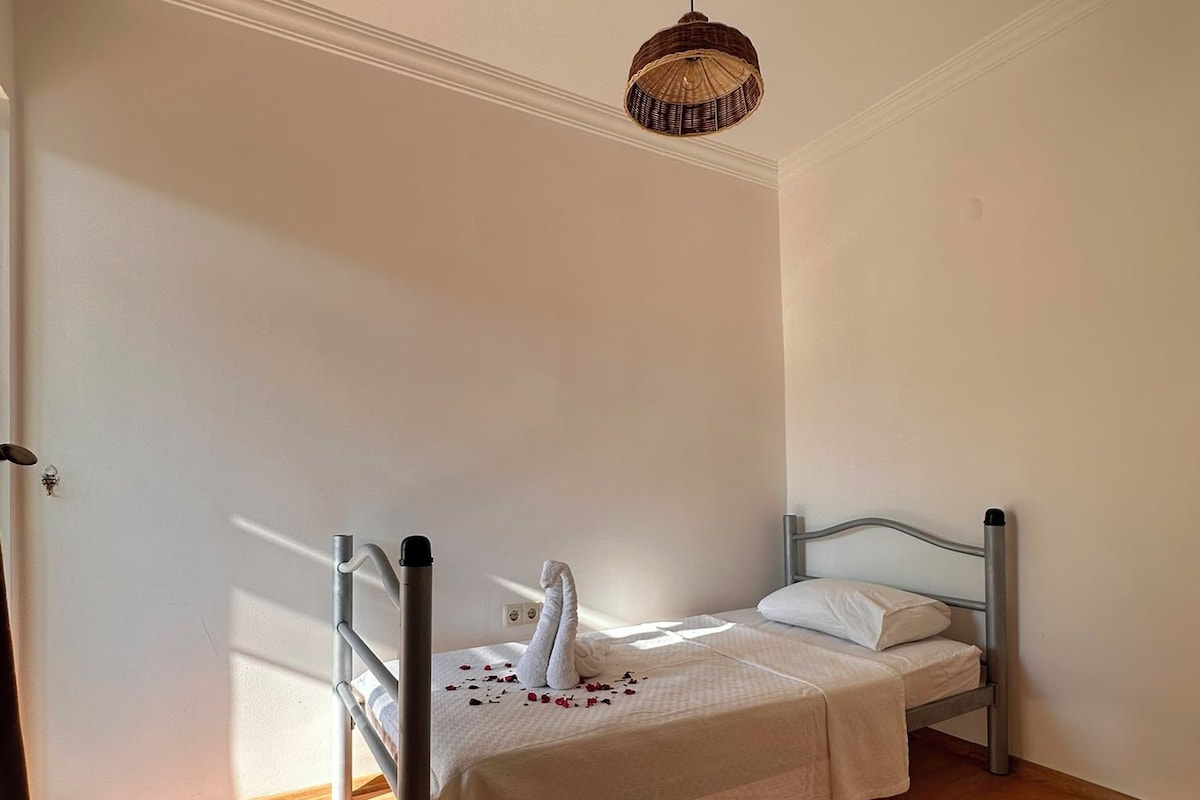 Quarto com cama, luminária pendente e piso de madeira.